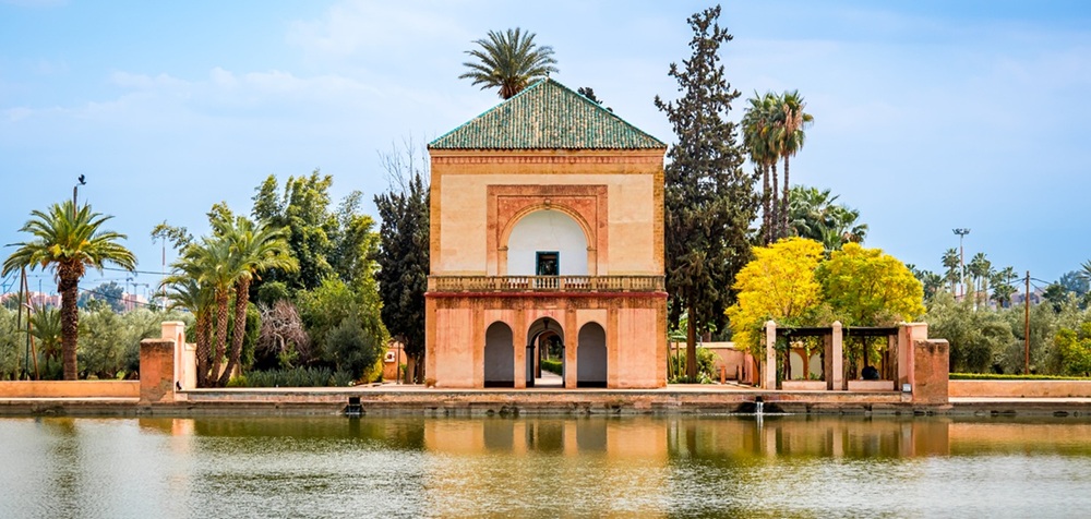 O pavilhão da Menara e o jardim da Menara em Marrakech, Marrocos, com palmeiras exuberantes, jardins vibrantes e reflexos na piscina Menara sob um céu azul claro, um ponto de referência famoso e um destino de viagem.
